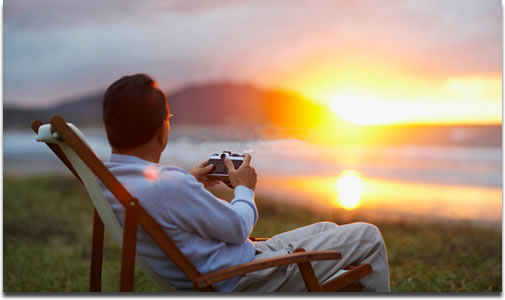 男性が夕日を眺めカメラを手に座っている画像